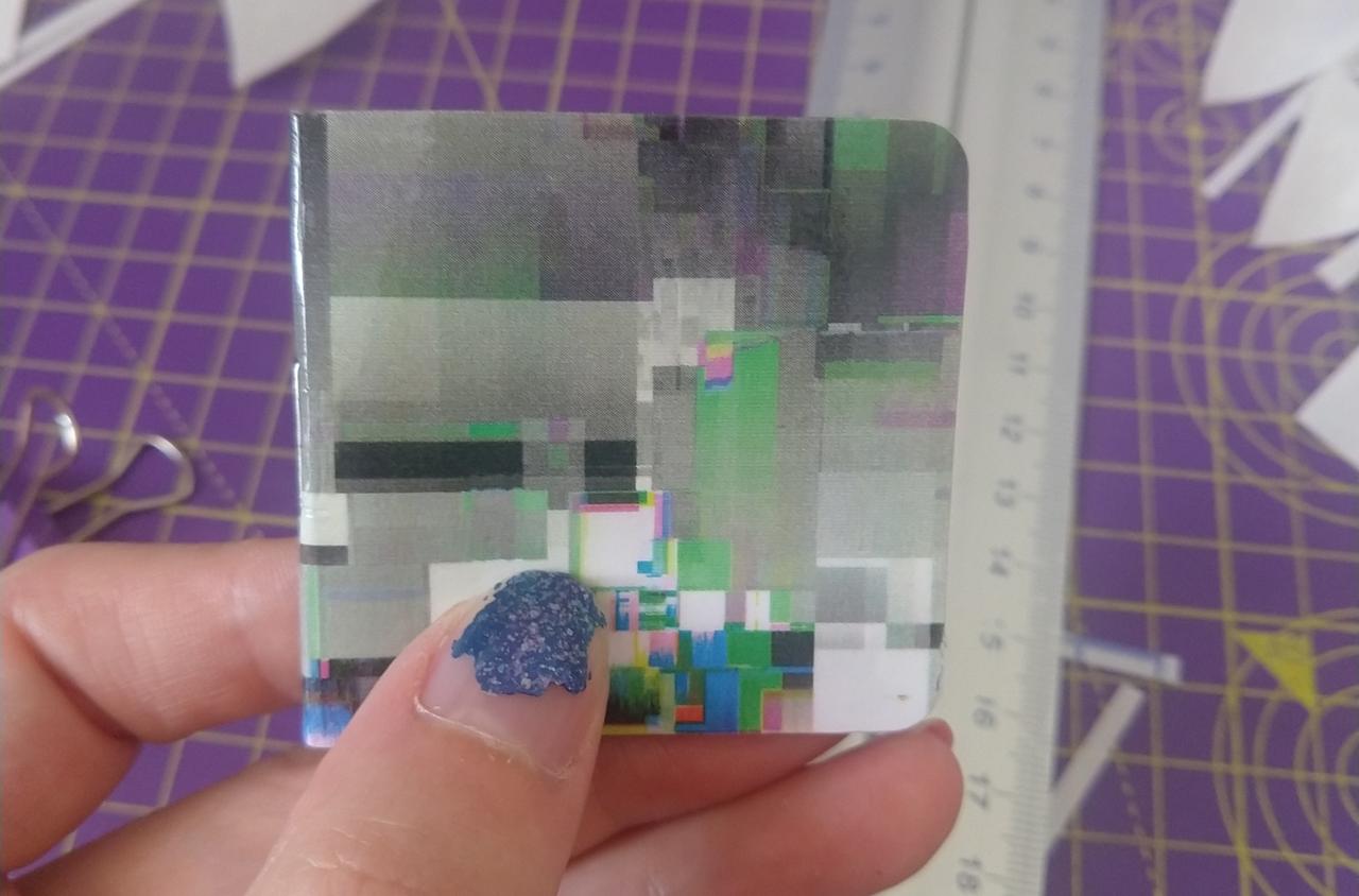 My fingers, holding a tiny sticker album with a colorful glitchart cover